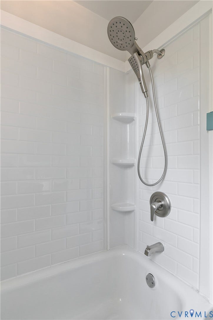 2207 Locbury Lane, Henrico, VA 23228 Bathtub and shower enclosure featuring white subway tile surround, integrated shelving, and brushed metal fixtures with a handheld showerhead
