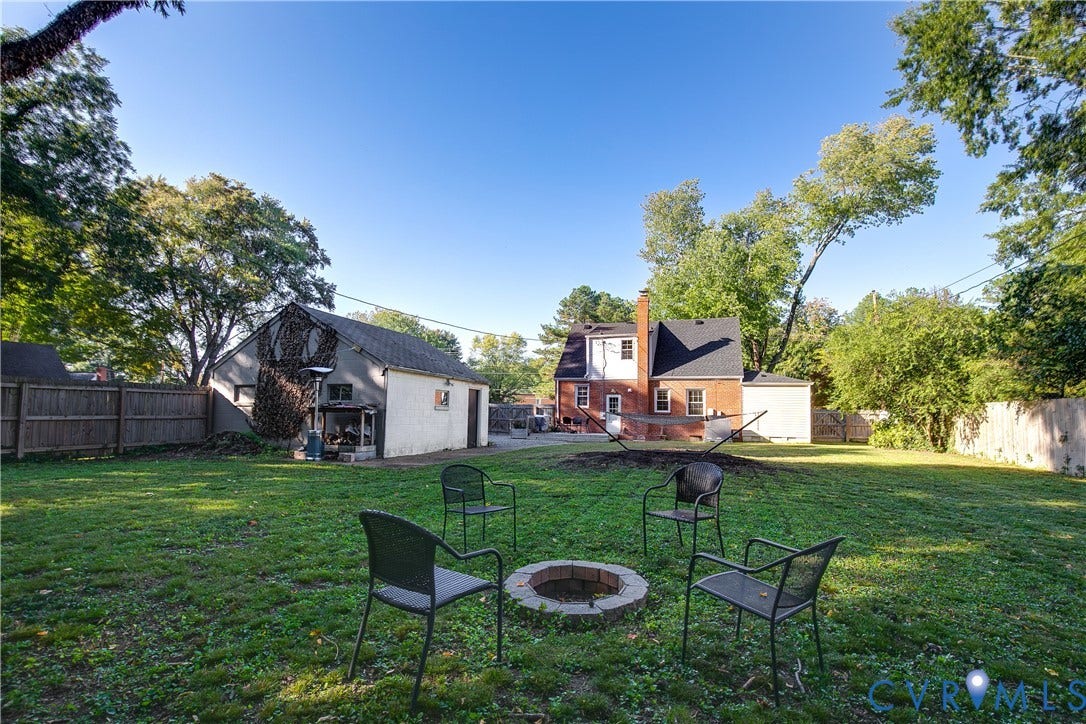 2207 Locbury Lane, Henrico, VA 23228 Expansive backyard featuring a stone fire pit, detached garage, brick exterior, and wooden privacy fencing