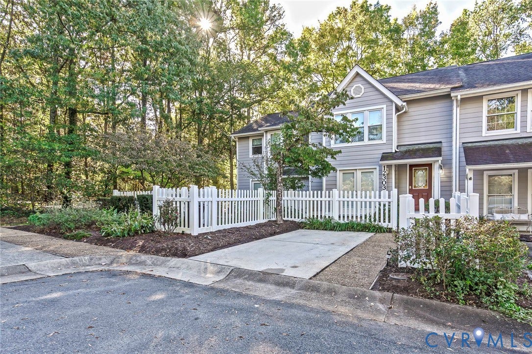 Multi-level exterior featuring horizontal siding, a private white picket fence, concrete driveway, and ornamental landscaping