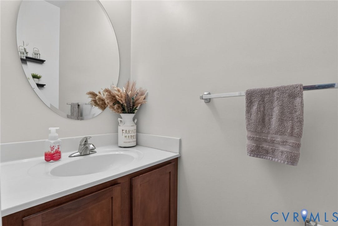 6852 Watch Harbour Circle, Hayes, VA 23072 Oval vanity mirror, integrated sink, chrome faucet, white countertop, and wood-finish cabinetry