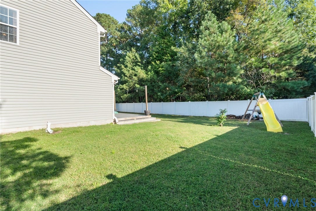 6852 Watch Harbour Circle, Hayes, VA 23072 Expansive grassy yard featuring a white privacy fence, mature trees, and a concrete patio