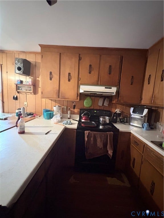 Kitchen featuring wood paneling, wood cabinetry, white countertops, and a black range