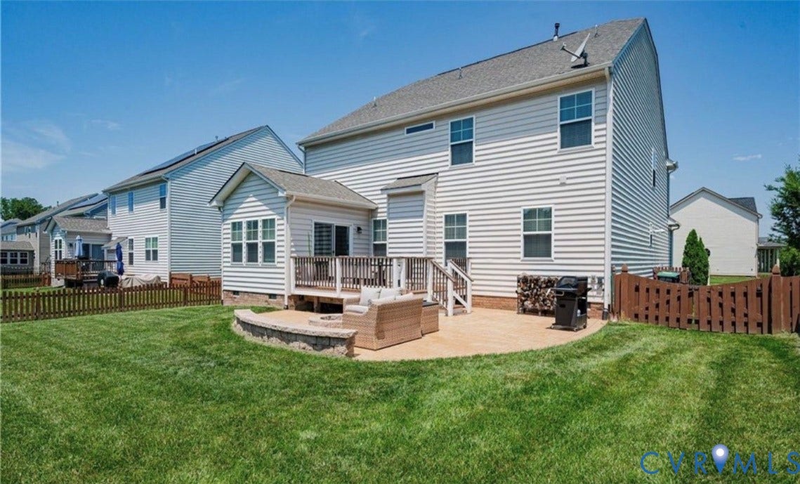 16001 Lost Crop Drive, Moseley, VA 23120 Expansive backyard featuring a manicured lawn, a wooden deck, a curved paved patio, and a privacy fence