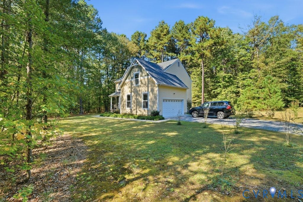 2490 Mountain Road, Glen Allen, VA 23060 Two-story residence featuring yellow vinyl siding, a gabled roofline, an attached single-car garage, and a gravel driveway, situated on a wooded lot