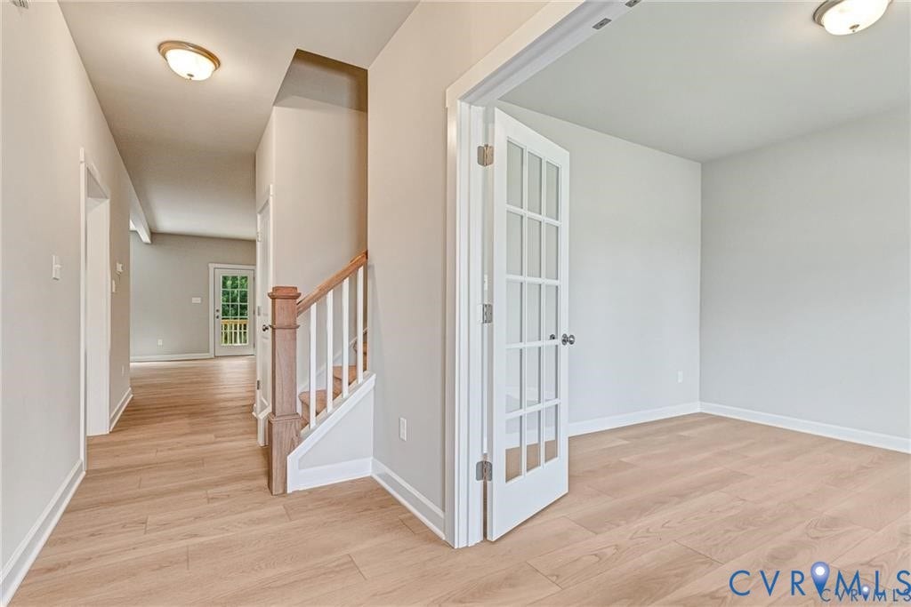Light wood-finish flooring throughout, white trim, and a white spindle staircase with wood handrail