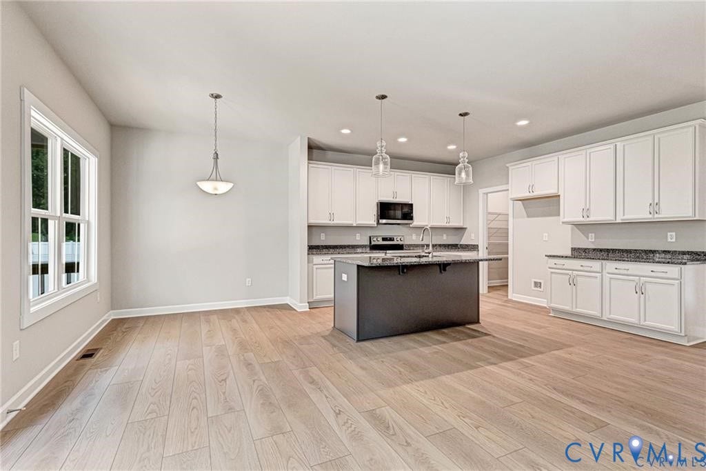 Open concept kitchen with wood-finish flooring, white cabinetry, dark stone countertops, and a central island