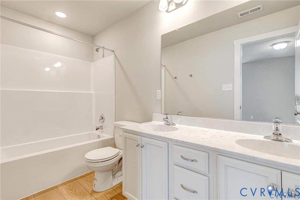 Dual sink vanity with white cabinetry and chrome hardware, a white countertop, and wood-finish flooring
