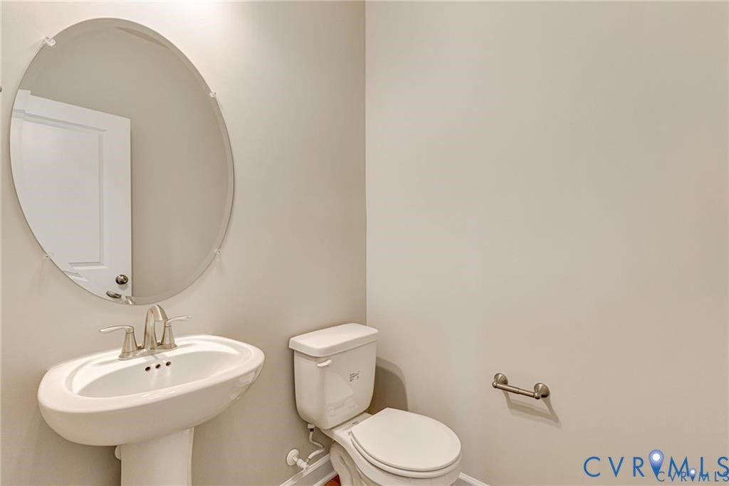 Pedestal sink with brushed nickel faucet, oval frameless mirror, and commode