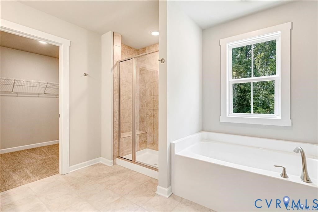 Freestanding soaking tub with brushed nickel fixtures, tiled walk-in shower with glass enclosure and built-in bench, neutral tile flooring, and a large window providing ample natural light