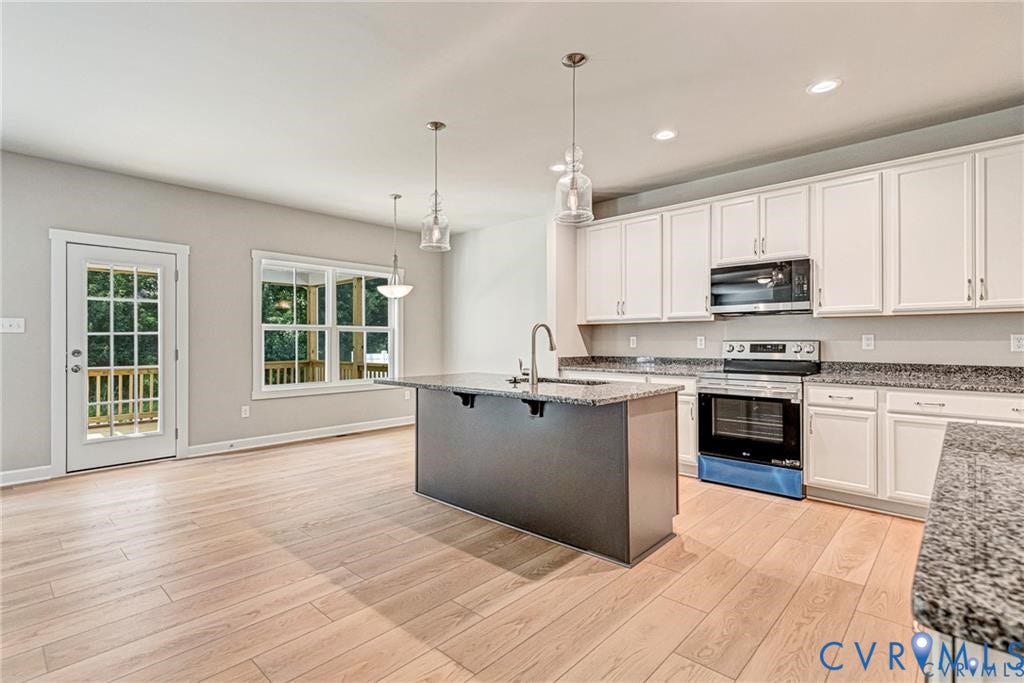 Open-concept kitchen with light wood-finish flooring, white cabinetry, dark stone countertops, and a central island with an integrated sink