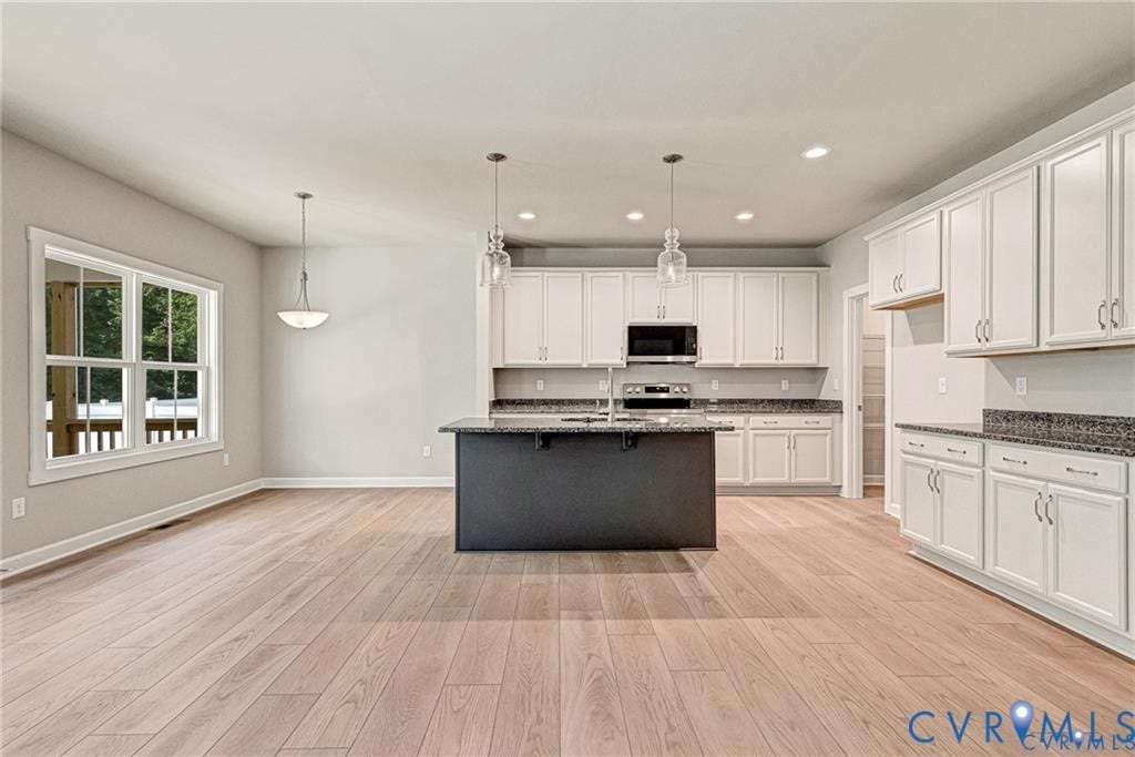 Open-concept kitchen with wood-finish flooring, white cabinetry, dark granite countertops, and a central island