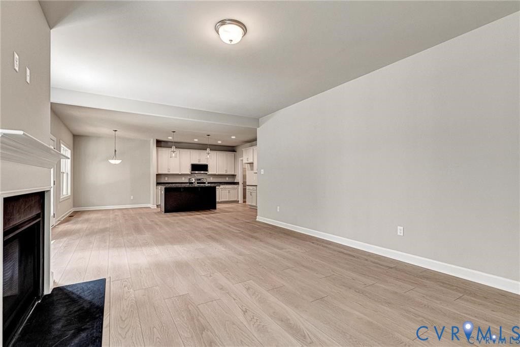 Open-concept living area with wood-finish flooring, a fireplace with a white mantel, and neutral wall tones