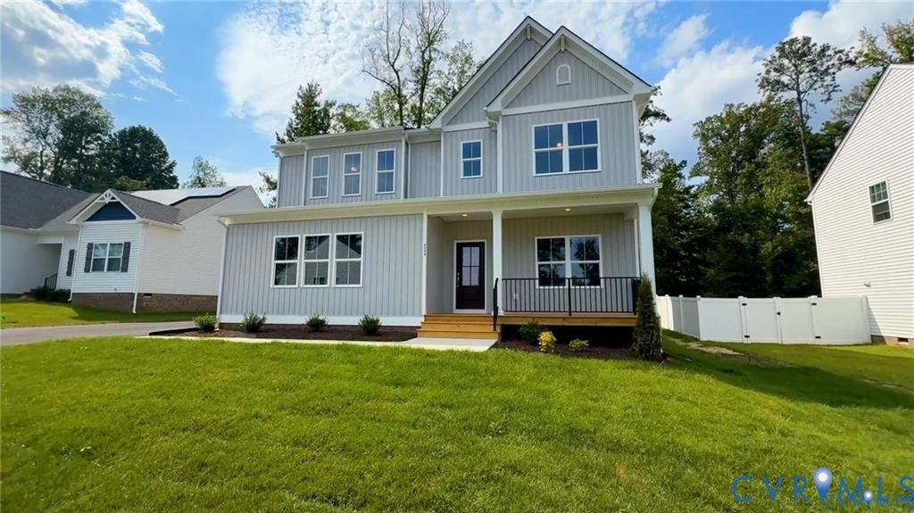 Light gray siding exterior with white trim, covered front porch with black railings, asphalt shingle roof, and a mature treeline