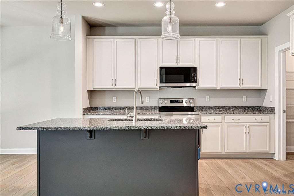 Kitchen featuring an expansive island, light-toned cabinetry, stainless steel appliances, and wood-finish flooring