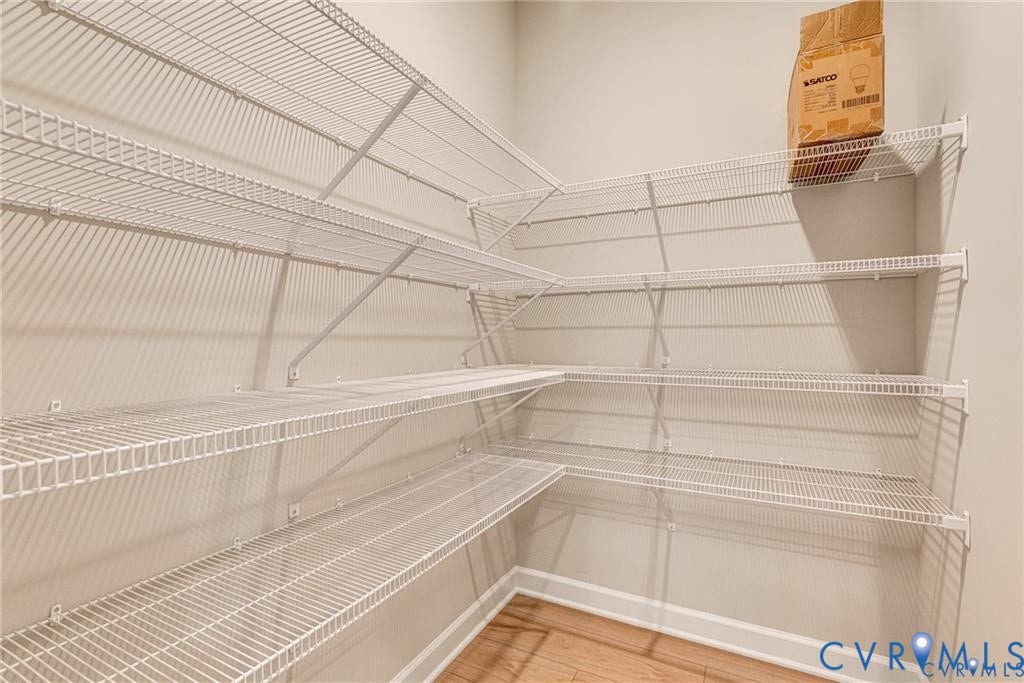Spacious pantry or storage closet featuring multiple wire shelving units with adjustable shelves for flexible organization, hardwood flooring, and bright natural lighting from overhead fixtures