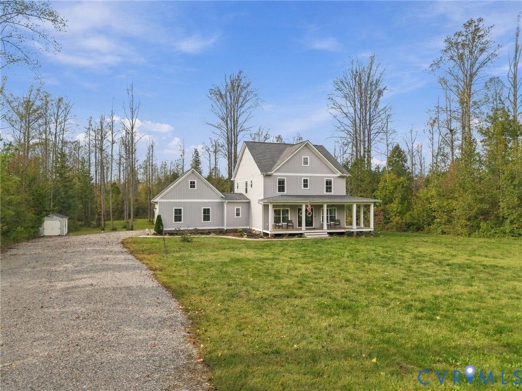 Two-story residence featuring light gray siding, a covered front porch, a multi-gabled roofline, a gravel driveway, and a detached storage shed on an expansive lot