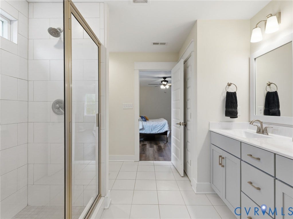 Bathroom featuring a glass-enclosed shower with white tiled walls, light gray vanity cabinet with a rectangular undermount sink, stone-surface countertop, and wall-mounted vanity light fixture