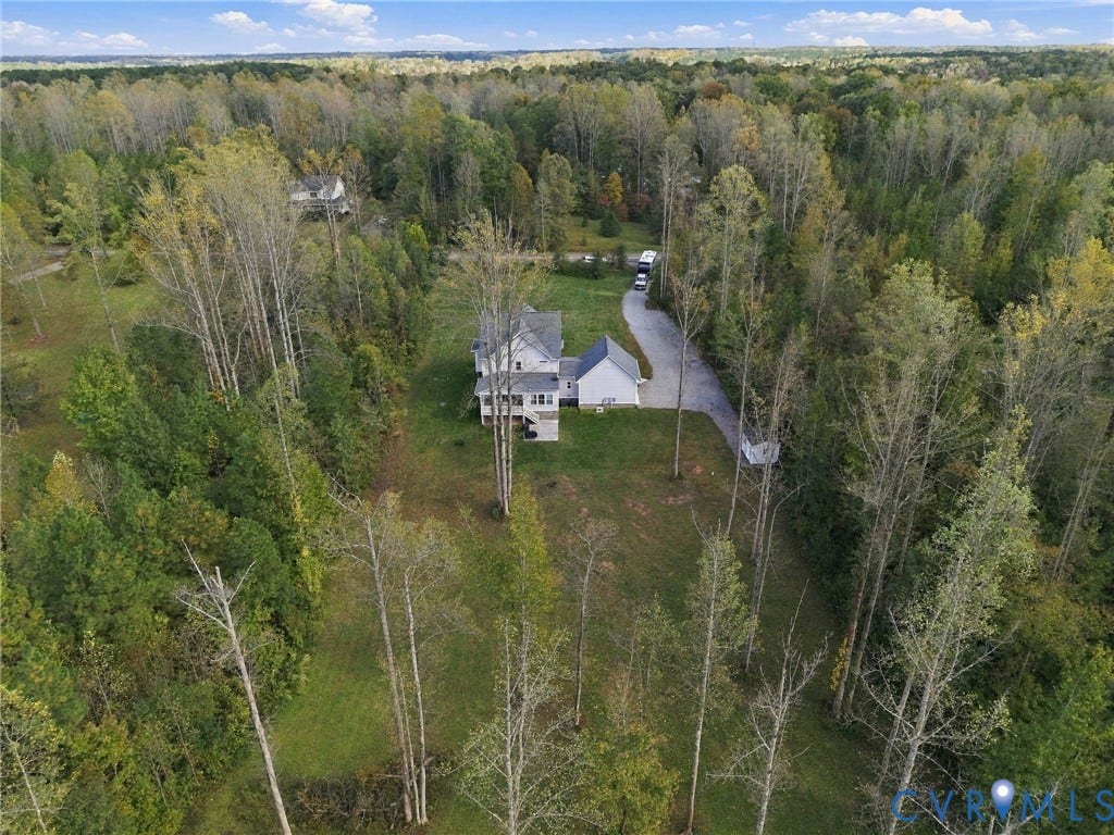 Multi-level residence featuring a multi-pitched roofline, light-toned exterior siding, an attached garage, and a long gravel driveway, all situated on a expansive, wooded lot