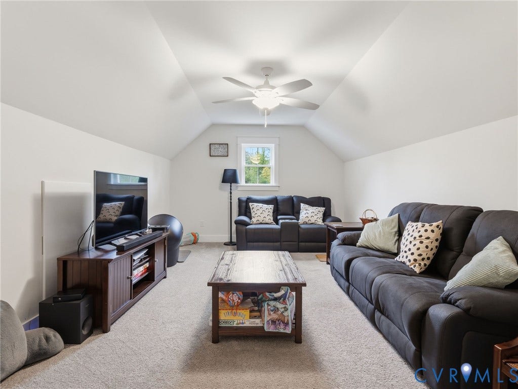 Vaulted ceiling featuring a central multi-blade ceiling fan and a single window