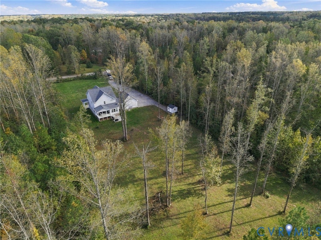 Expansive lot featuring mature woodlands, a multi-story residence with a covered porch, an asphalt driveway, and a detached storage structure