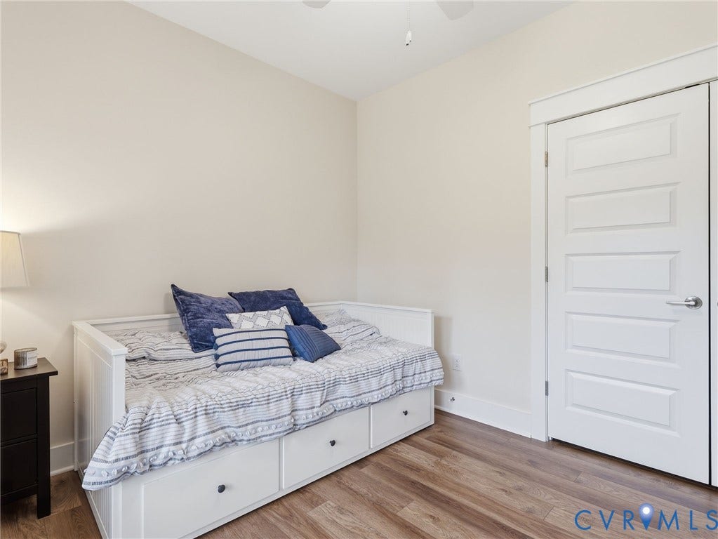 Neutral-toned interior featuring wood-finish flooring, a five-panel interior door with crisp trim, and a ceiling-mounted fan