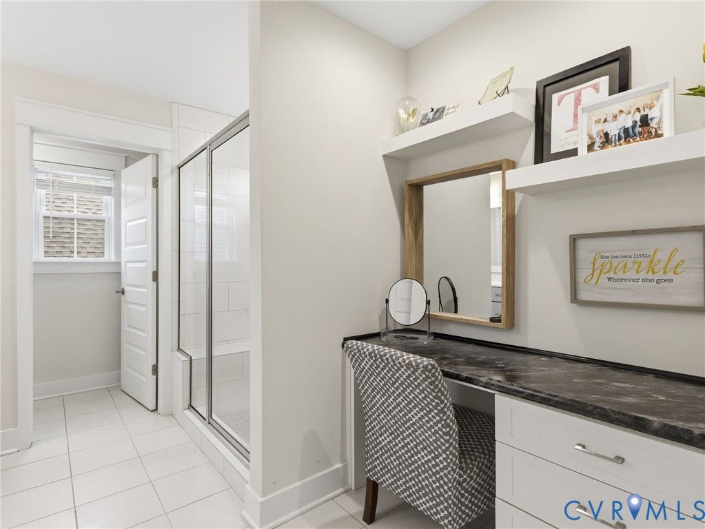Built-in vanity with stone-finish countertop and white cabinetry, glass-enclosed shower with tiled interior, and floating wall-mounted shelving