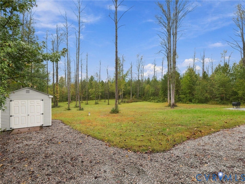 Expansive grounds featuring a vinyl-sided storage shed, gravel surfaces, and mature trees