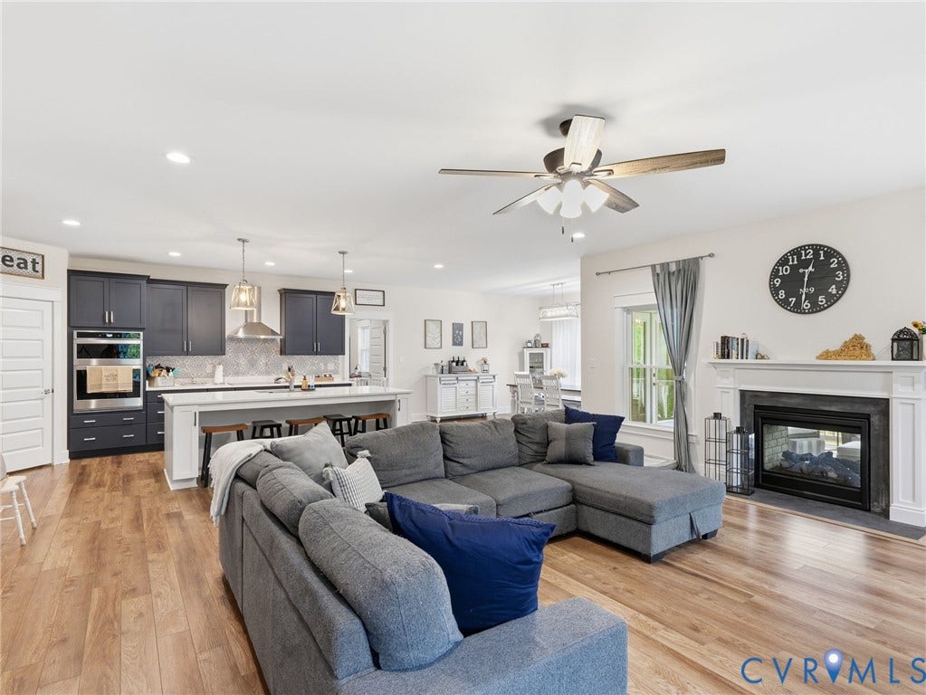 Open-concept kitchen featuring dark cabinetry, an island with seating, a built-in wall oven, and wood-finish flooring, complemented by a fireplace with a decorative mantel