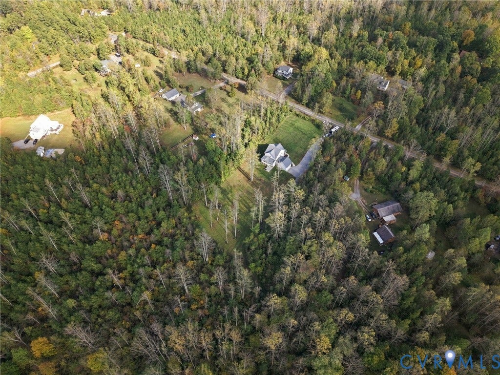 Aerial perspective of a sprawling parcel featuring dense mature woodland, expansive cleared acreage, a paved driveway, and detached storage structures