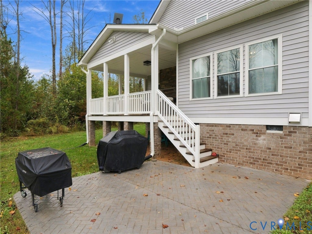 Covered back porch featuring light gray horizontal siding, a stone fireplace, white railings, and a stamped concrete patio