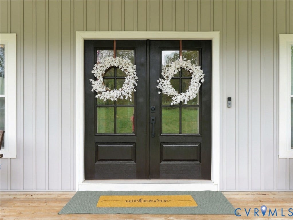 Double entry doors featuring six-light glass panels and dark finish hardware, set against light gray vertical board-and-batten siding
