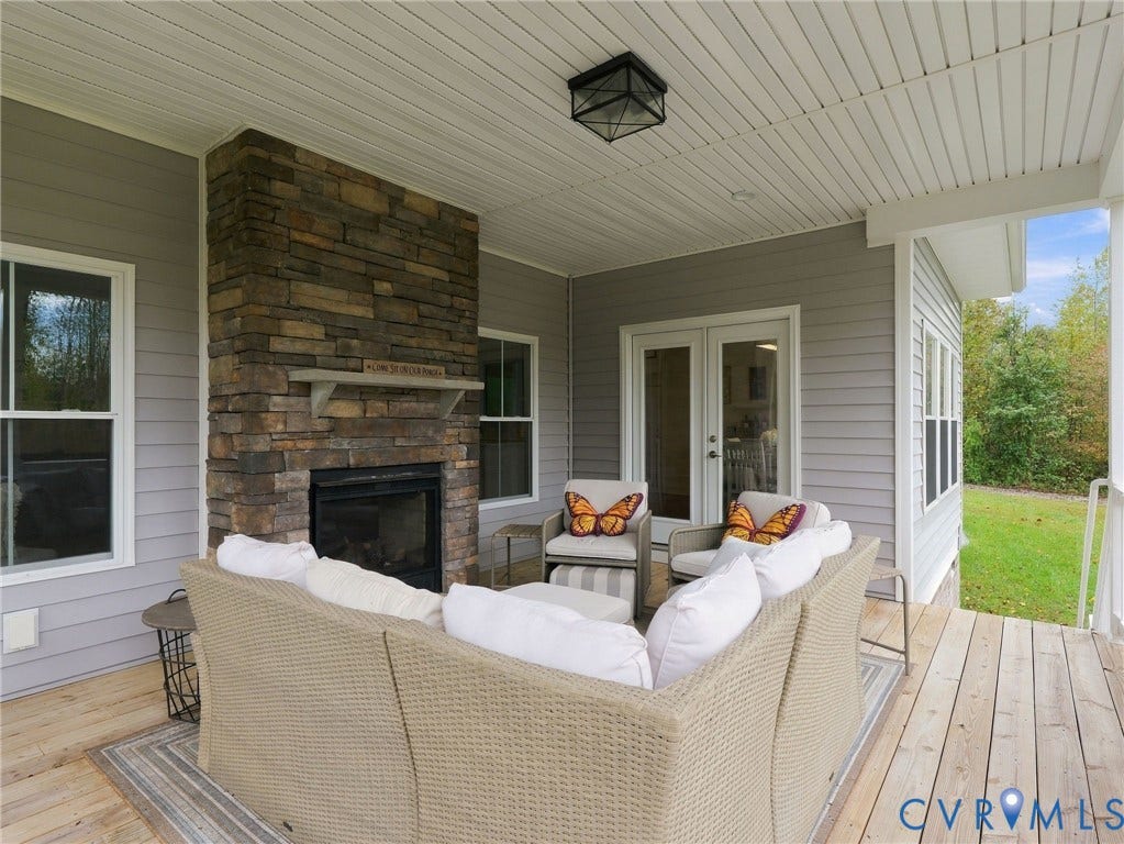 Covered patio featuring wood-finish decking, an exterior stacked-stone fireplace, a wood mantel, and double-door entry