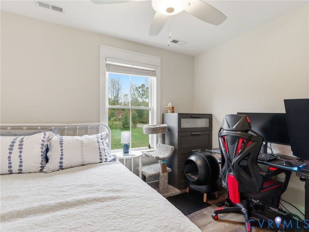 Neutral-toned room featuring a single-hung window with casing, wood-finish flooring, and a ceiling-mounted light fixture with integrated fan
