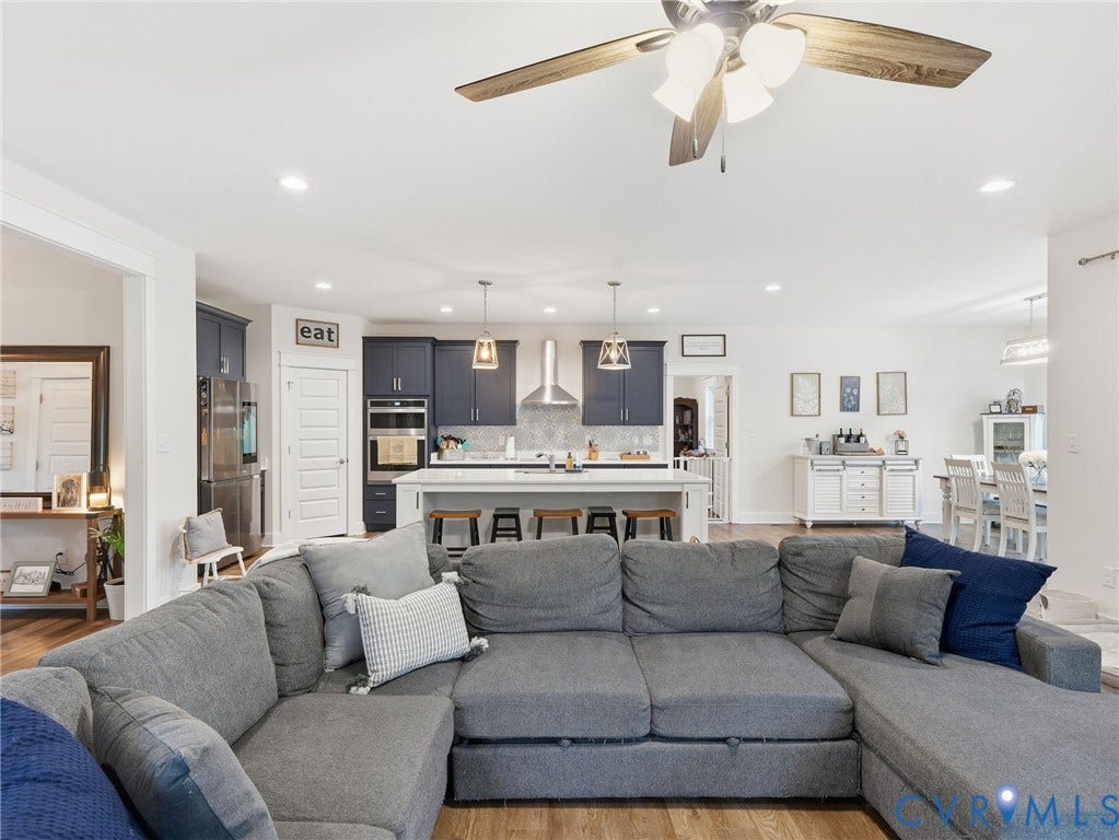 Open-concept kitchen featuring dark-toned cabinetry, a central island with bar seating, stainless steel appliances, a stainless steel range hood, and recessed lighting