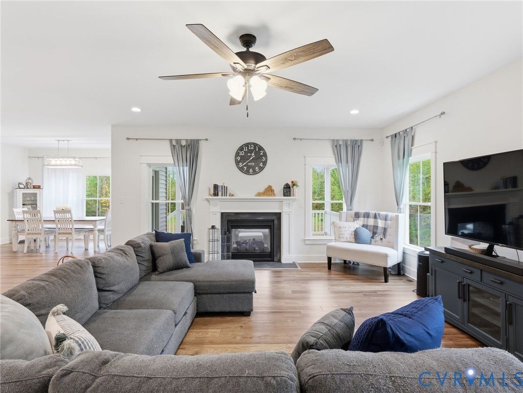 Living area featuring wood-finish flooring, a fireplace with a white mantel, and a ceiling fan with integrated lighting