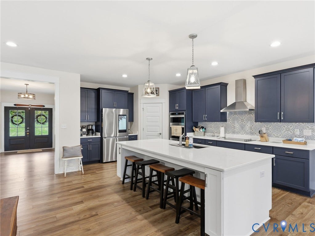 Kitchen featuring deep blue shaker-style cabinetry, white quartz countertops, central island, patterned tile backsplash, and stainless steel appliances