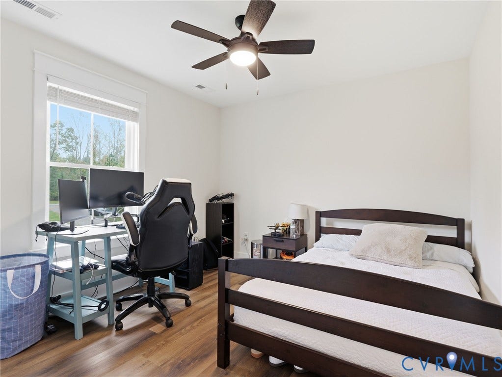 Room featuring wood-finish flooring, a ceiling-mounted light fixture with fan, and a window with white trim