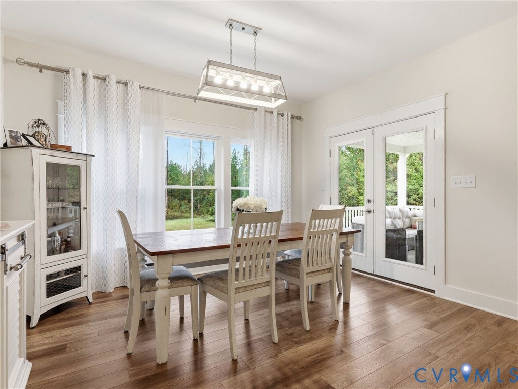 Dining area featuring wood-finish flooring, a rectangular metal-frame pendant light, large double-pane windows, and glass-paneled double doors providing access to an exterior porch