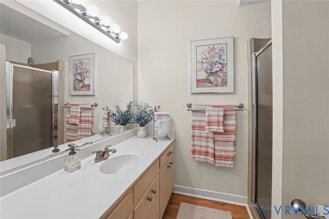 4815 Woodbriar Court, Midlothian, VA 23112 Full-width vanity with solid surface countertop, integrated sink, wood-finish cabinetry, expansive wall-mounted mirror, and glass-enclosed shower