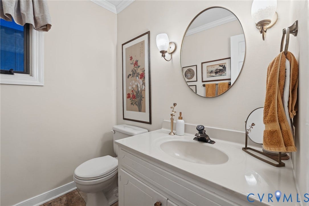 4815 Woodbriar Court, Midlothian, VA 23112 Bathroom vanity featuring a solid-surface countertop with an integrated basin, oval mirror, dual wall-mounted light fixtures, and a dual-handle faucet