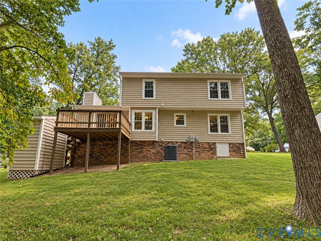 Rear elevation featuring beige horizontal siding, a wood deck, a brick foundation, and multiple windows
