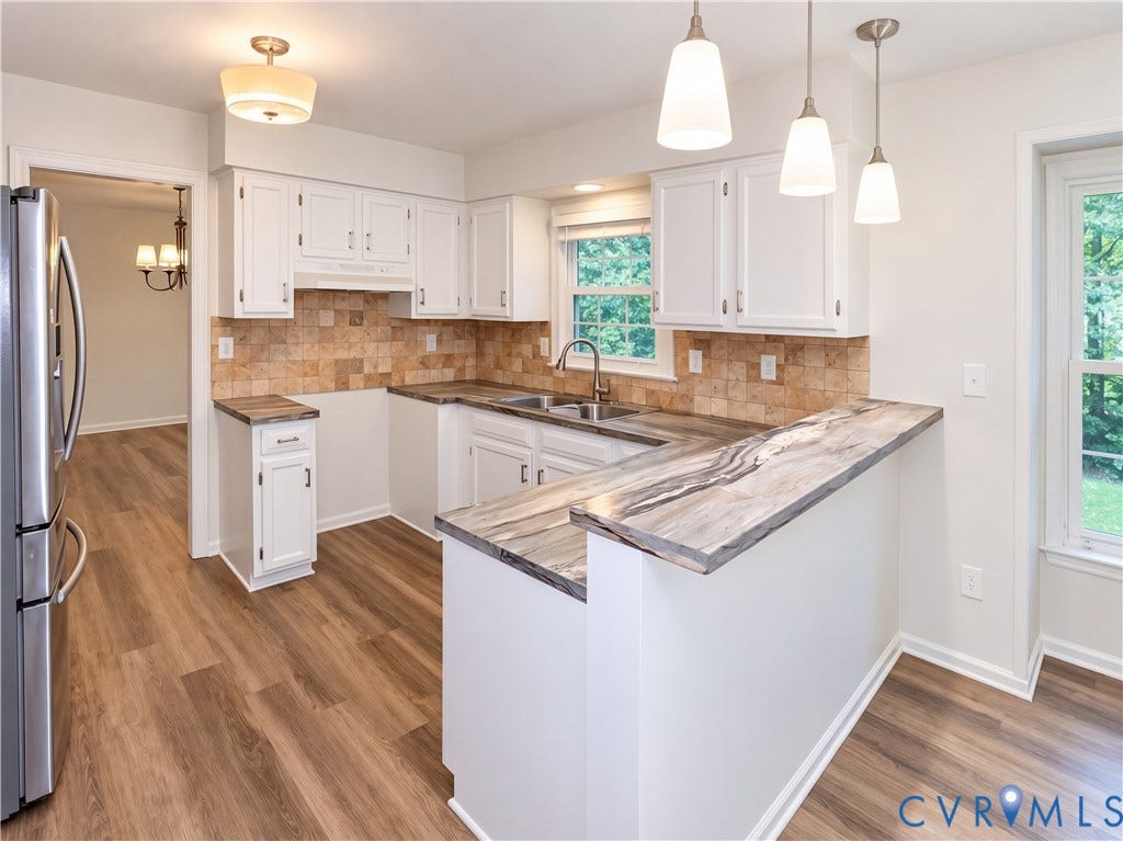 Kitchen featuring wood-finish flooring, white cabinetry, integrated stainless steel refrigerator, and a breakfast bar with a patterned countertop
