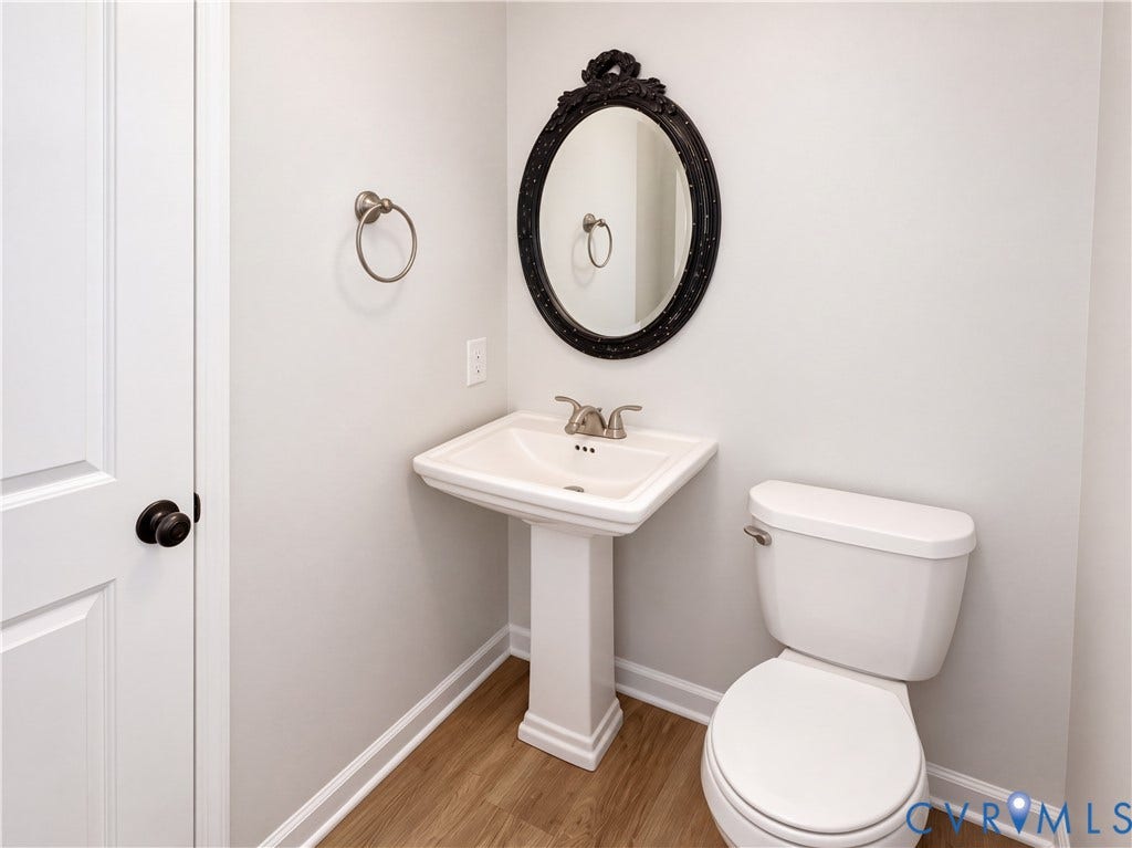 Pedestal sink with a dual-handle faucet, oval framed mirror, and wood-finish flooring