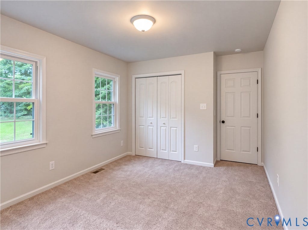 Neutral wall paint, carpet flooring, two sash windows, bi-fold closet doors, and a paneled door with a round black knob