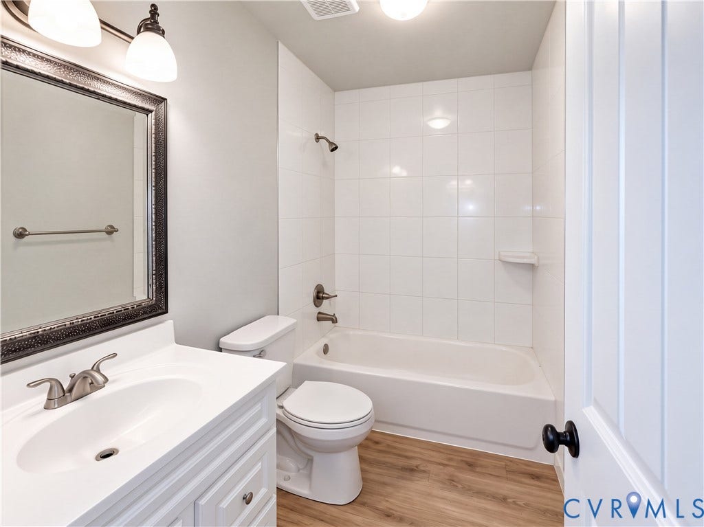 Bright, updated bathroom featuring a ceramic tile shower surround with integrated tub, white vanity with dual-handle faucet, framed mirror with decorative trim, recessed ceiling lighting, and wood-finish flooring