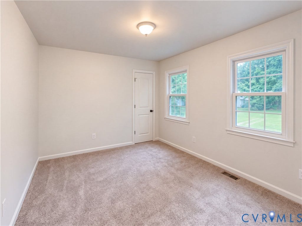 Neutral tone wall paint, neutral tone carpeting, two paneled windows with natural light, white trim, and a flush mount ceiling light