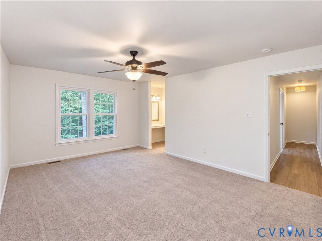 Spacious primary living area featuring neutral carpeting, ceiling fan with integrated lighting, and abundant natural light from dual French doors