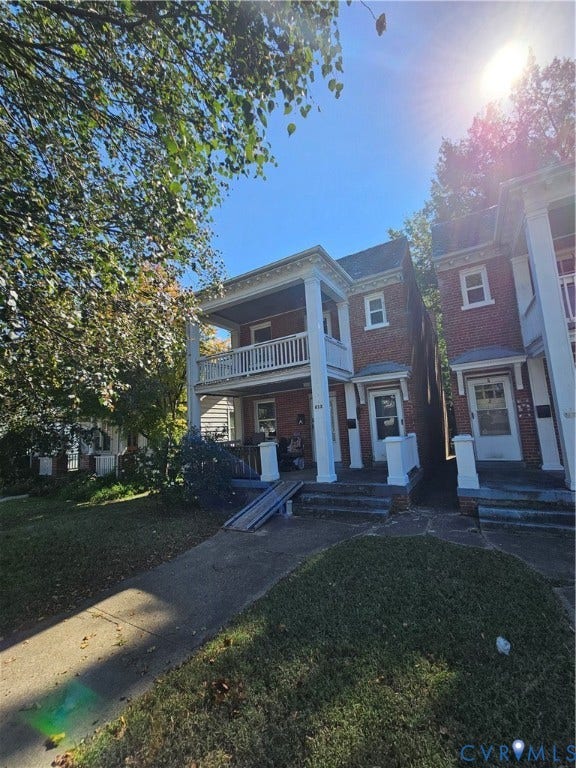 613 E Brookland Park Boulevard, #2, Richmond, VA 23222 Brick exterior with a white-railed upper balcony, covered lower porch with white pillars, and a concrete pathway leading to the entrance