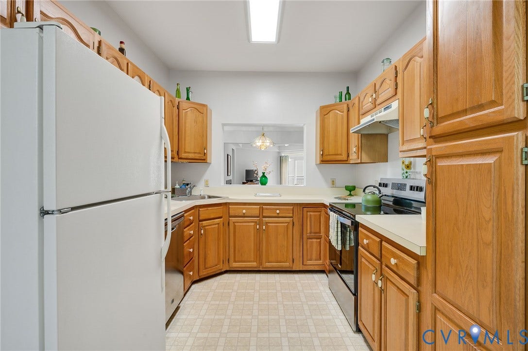 U-shaped kitchen featuring warm-toned wood cabinetry, solid-surface countertops, tile flooring, and a pass-through window