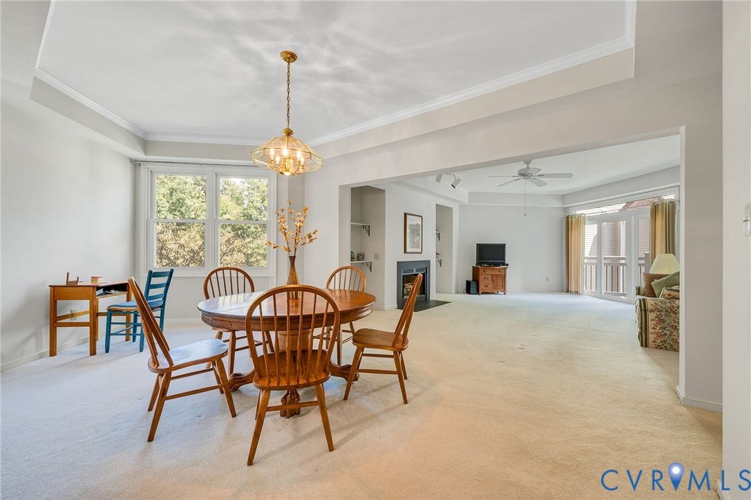 Tray ceilings, multi-pane windows, brass-finish hanging light fixture, fireplace with black surround, and glass panel doors